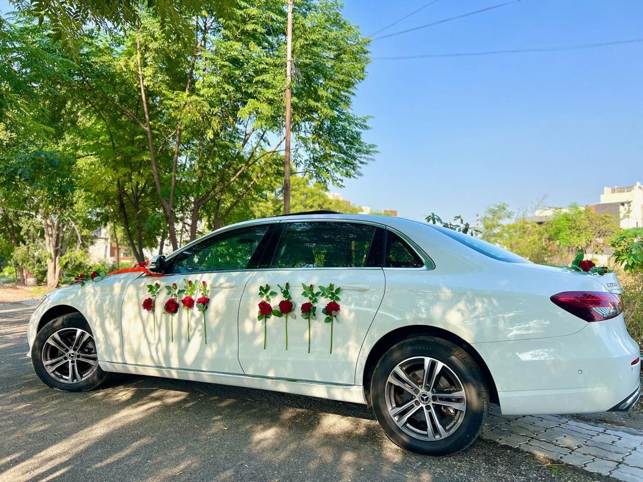 White Mercedes-Benz E-Class decorated with roses, parked under green trees